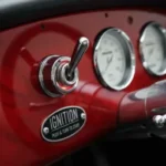Red classic car dashboard with chrome ignition toggle switch and analog gauges.