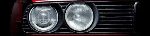 Close-up of dual round headlights on a vintage red car, illustrating the difference between candela and lumens in evaluating hot rod headlight output and visibility