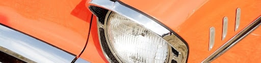Close-up of a chrome round headlight on an orange vintage classic car at a car festival, representing the housing type used in period-correct LED headlight upgrades