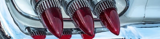 Close-up of three red cone-shaped taillights on a white vintage classic car at a car show, demonstrating the lens texture and diffusion that defines period-correct hot rod lighting